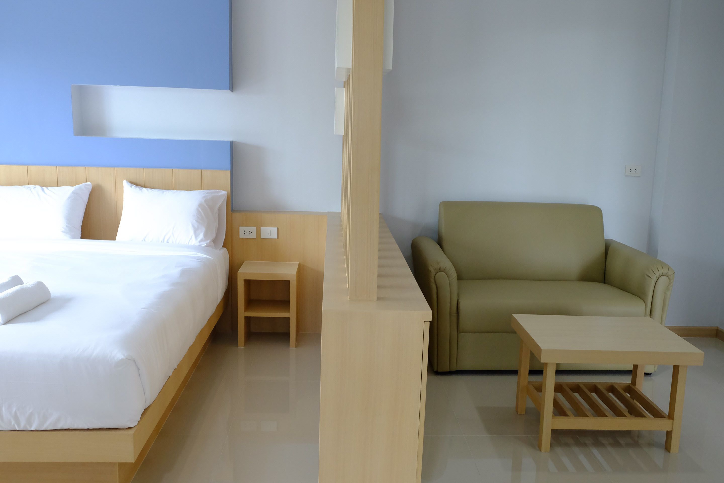 Ein Hotelzimmer mit einem Bett, einem kleinen Holztisch, einem grünen Sessel und einem hellen Couchtisch.