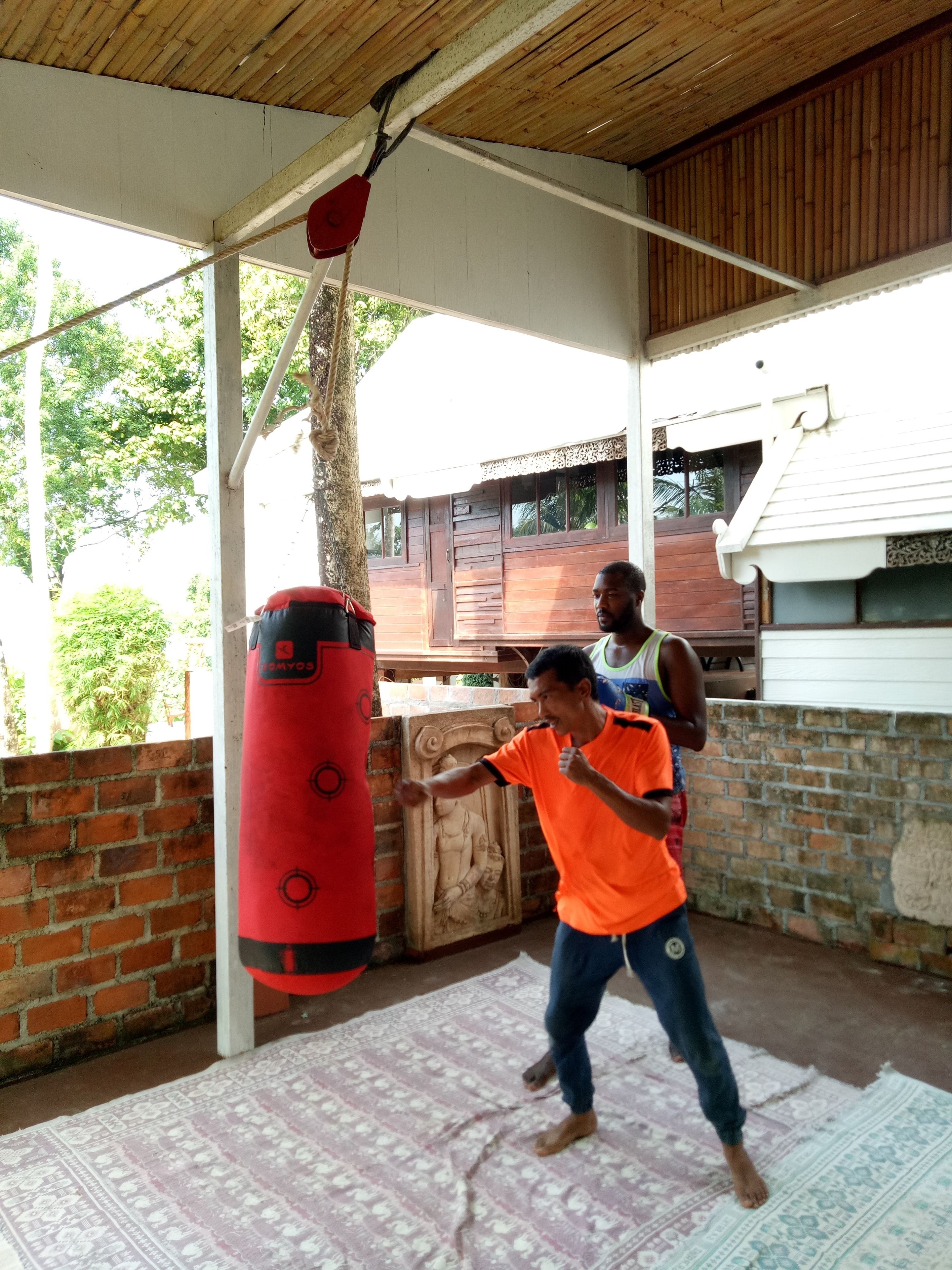 A covered outdoor area with a punching bag, a brick wall, and a patterned rug.
