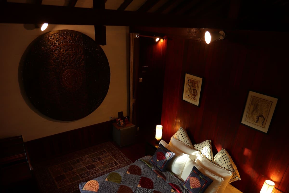 A dimly lit room with a bed, a wall-mounted circular decorative item, and two wall-mounted lamps.