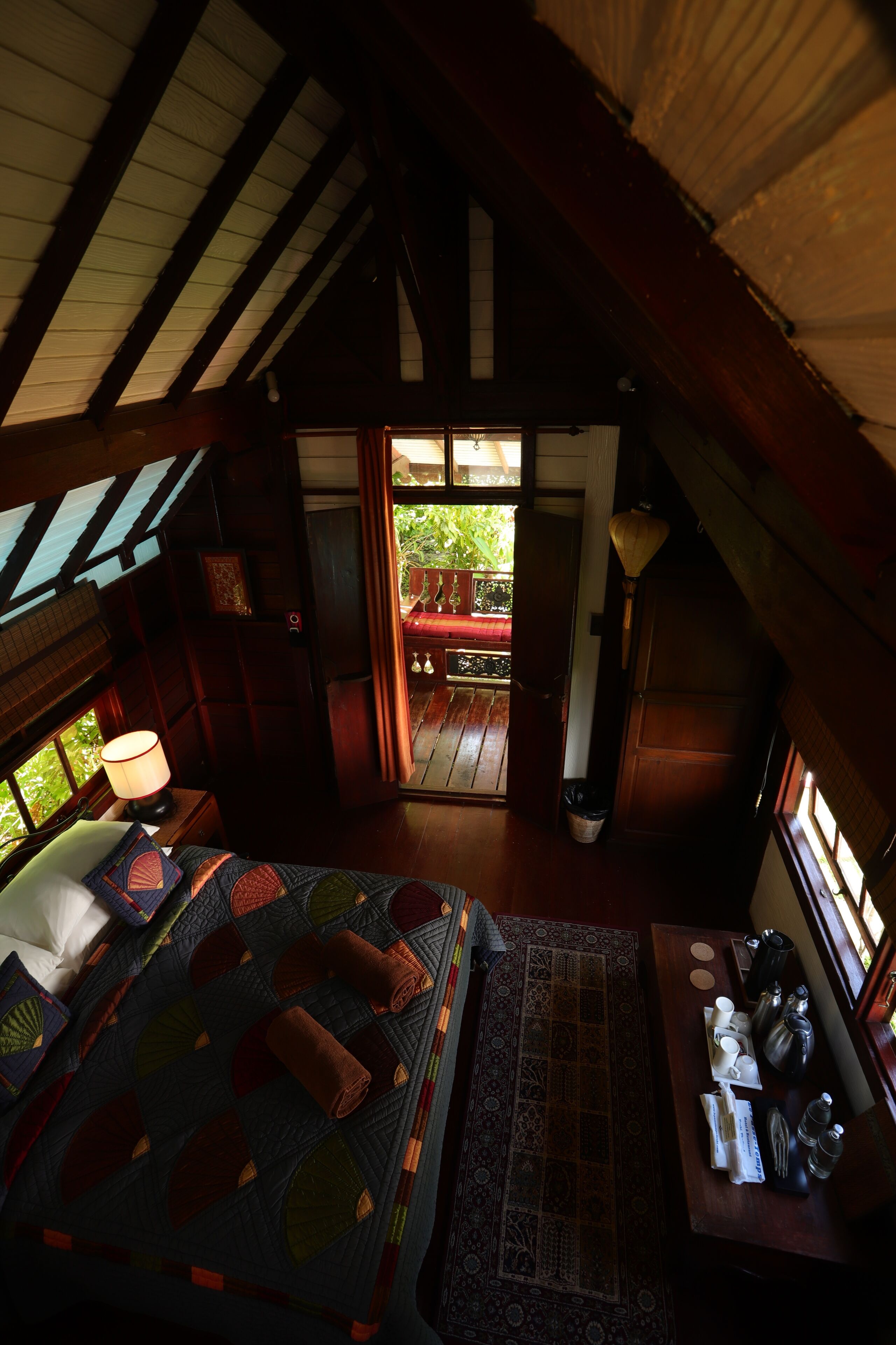 A cozy attic bedroom with a large bed, a wooden desk, and a view of the outdoors.