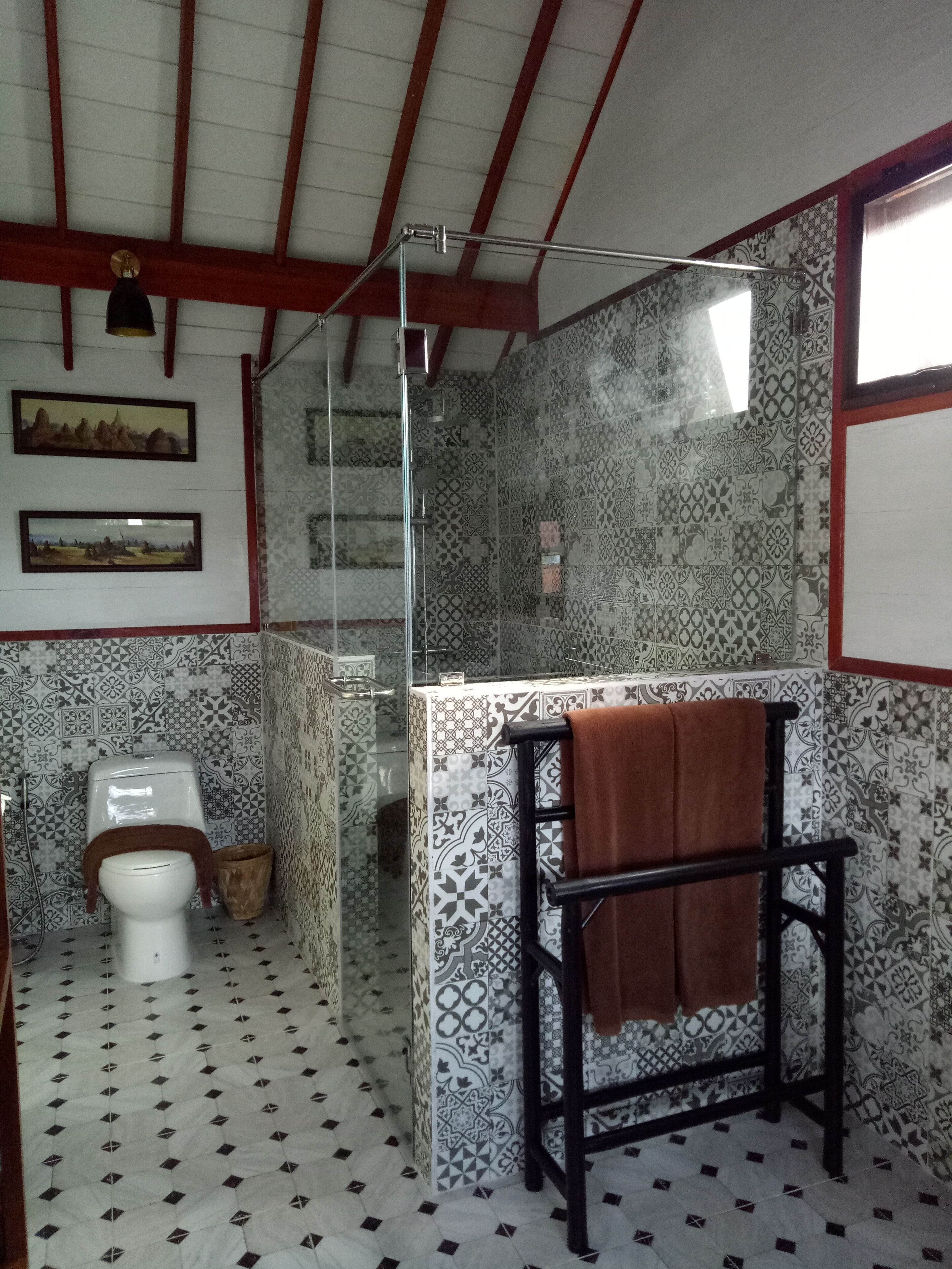 Un baño con baldosas estampadas, inodoro, ducha y perchero para toallas.