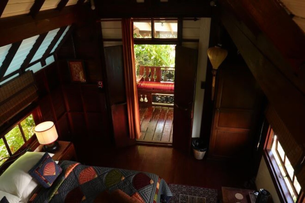 A cozy room with a bed, a lamp, and a view of a balcony with a red chair.