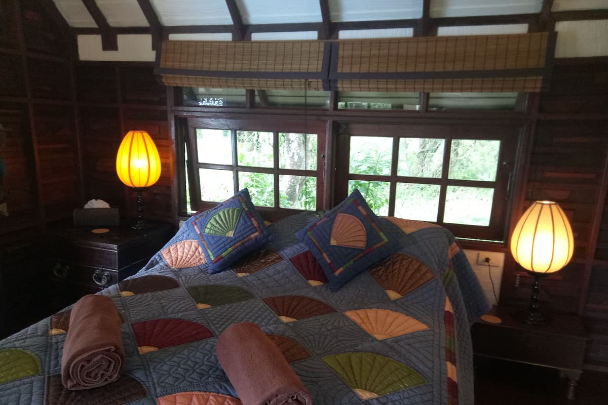 A bedroom with a large bed, two bedside lamps, a window with a view of trees, and a wooden headboard.
