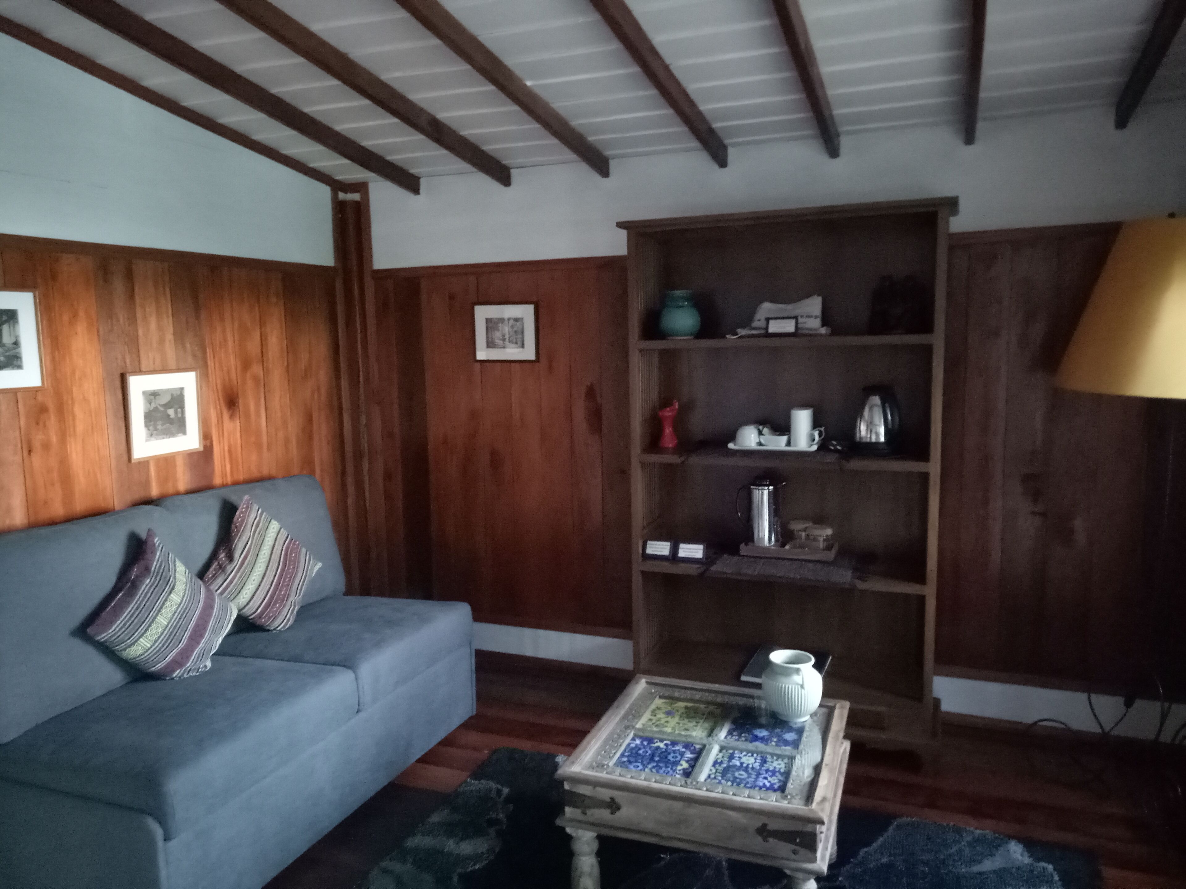Ein Wohnzimmer mit einem blauen Sofa, Holzvertäfelung, einem Couchtisch mit Fliesenplatte und einem Bücherregal.