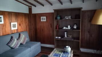 Ein Wohnzimmer mit einem blauen Sofa, Holzvertäfelung, einem Couchtisch mit Fliesenplatte und einem Bücherregal.
