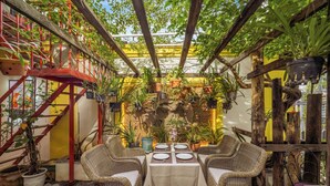 A cozy patio area with wicker furniture, a table set for dining, and various potted plants. - Pergola Hotel Design (Da Nang)