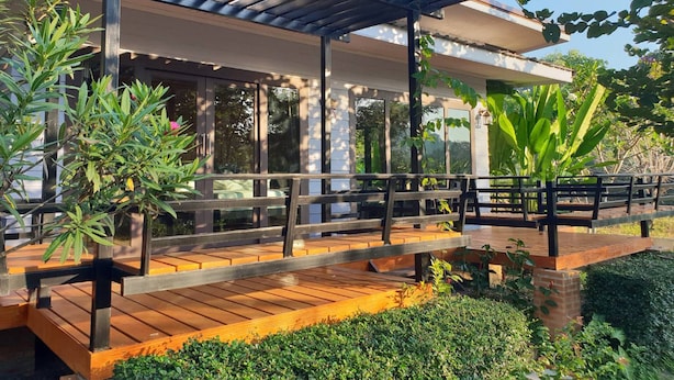 Een overdekte buitenruimte met houten banken en een pergola, omgeven door groen en planten.