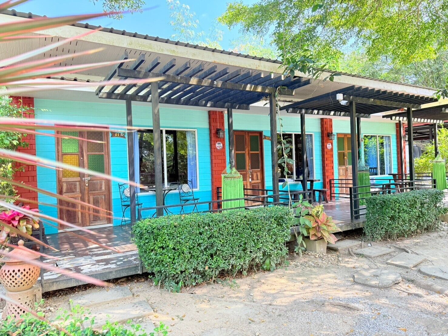 A colorful building with a covered patio area, a small garden, and a seating area with tables and chairs.