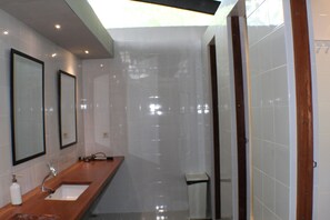 A modern bathroom with a wooden vanity, a large mirror, and a glass shower enclosure. - Kakatua Hostel (Waisai)