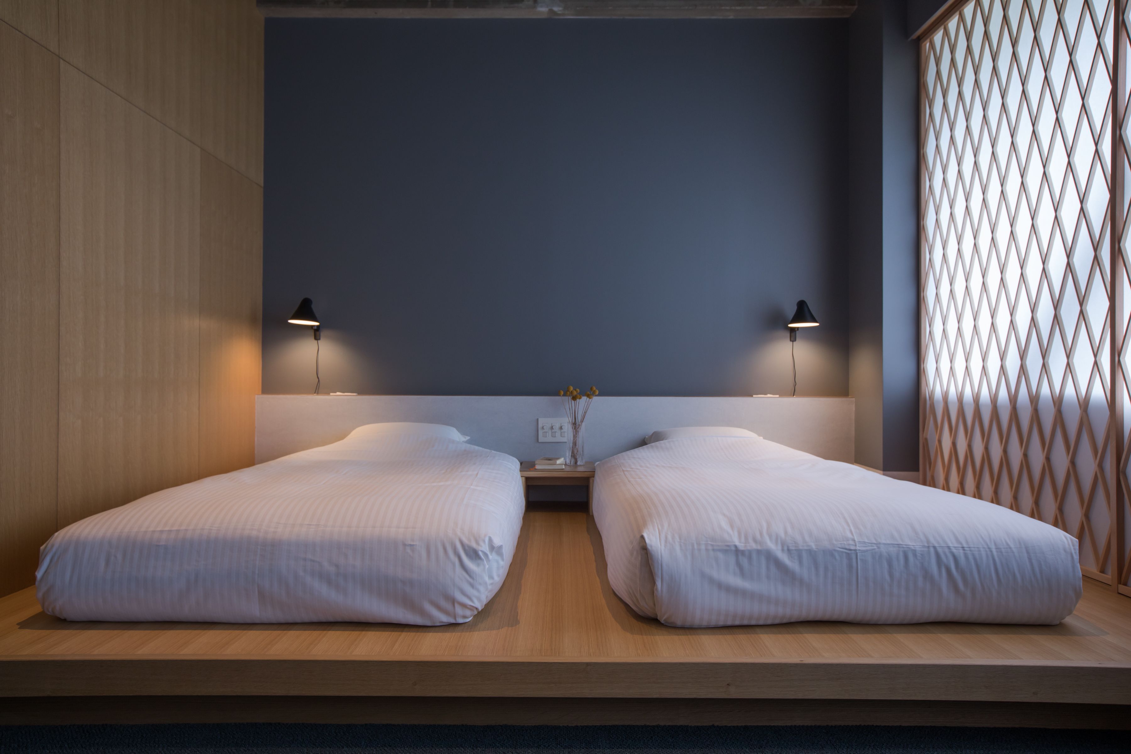 Un dormitorio moderno con dos camas individuales, una mesita de noche con un florero y un separador de celosía.