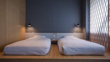 Un dormitorio moderno con dos camas individuales, una mesita de noche con un florero y un separador de celosía.