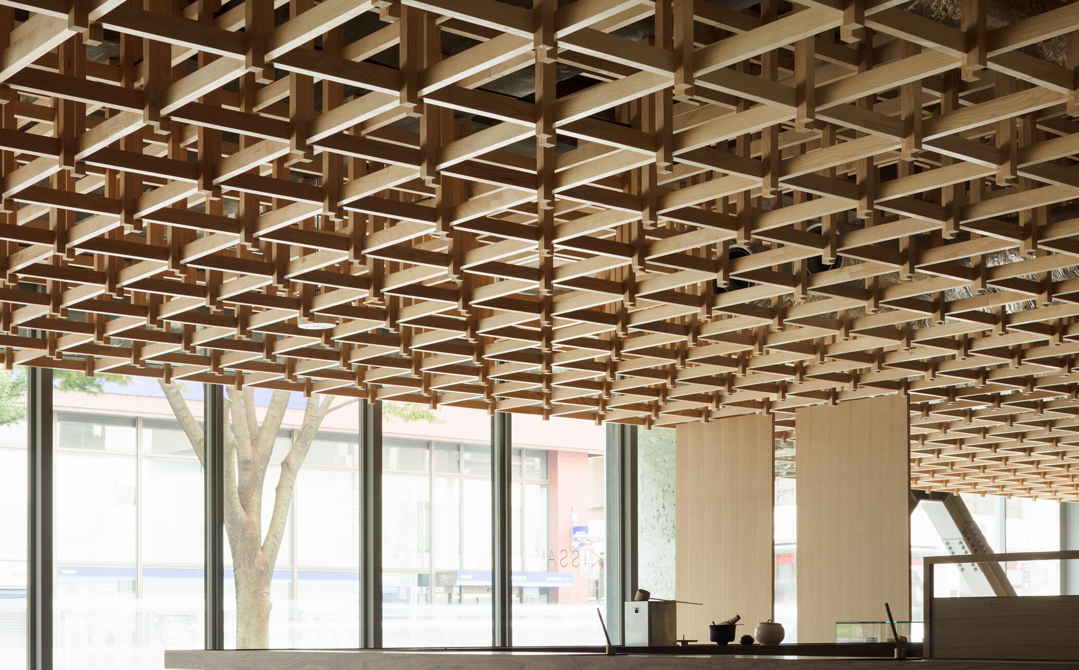 Un intérieur moderne avec une structure de plafond en bois aux motifs géométriques, de grandes fenêtres et un design minimaliste.