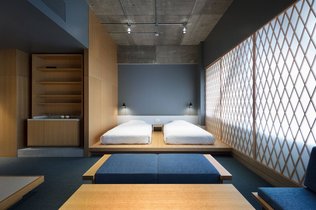 A modern hotel room with a bed, a small kitchenette, and a view through a lattice partition.