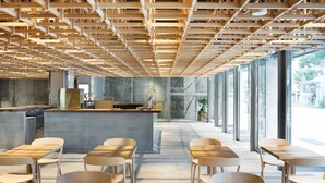 A modern cafe with wooden tables and chairs, a concrete counter, and large windows offering a view of the street. - KUMU Kanazawa by The Share Hotels (Kanazawa)