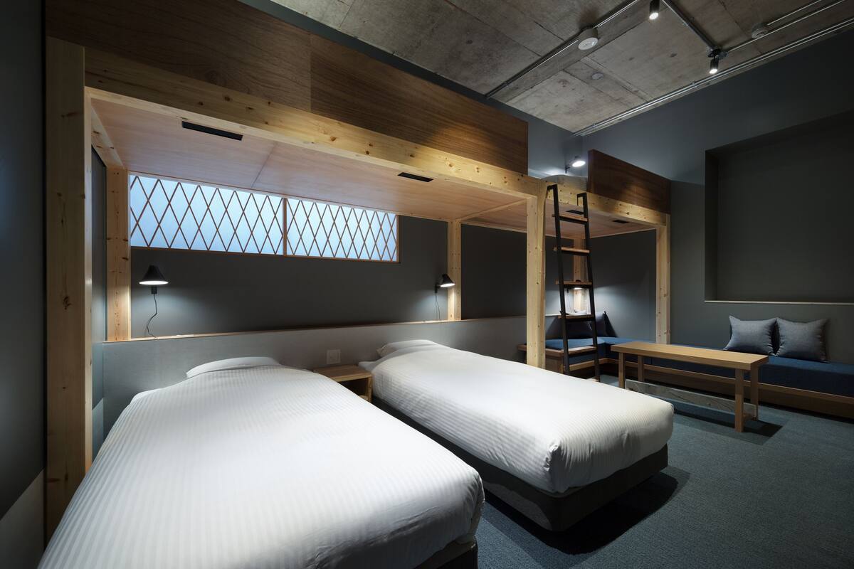 A modern room with two beds, a bench, a ladder, and a window with a geometric pattern.
