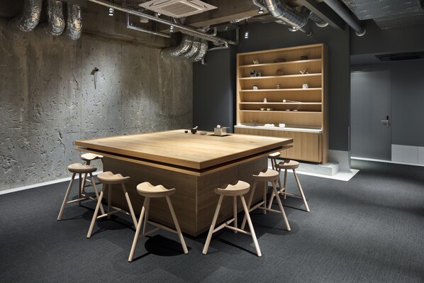 A modern meeting room with a large wooden table, four bar stools, and a built-in bookshelf.