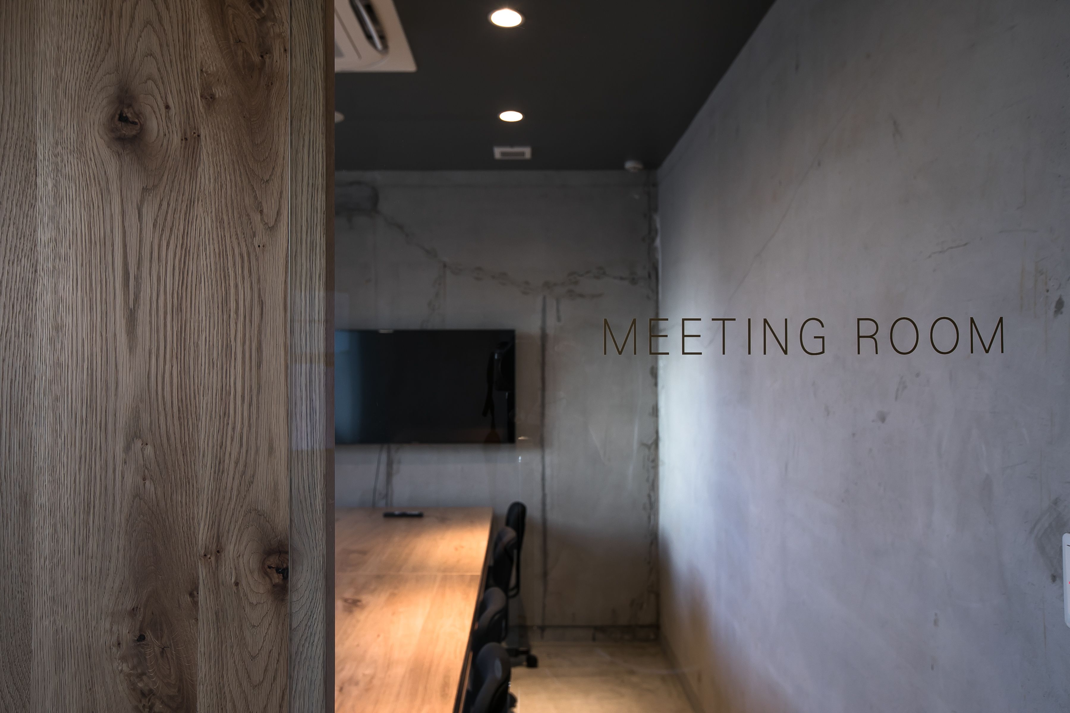 A meeting room with a wooden floor, a long table, and a large flat-screen TV.