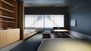A minimalist Japanese-style room with tatami flooring, a low wooden desk, a cushioned bench, and a large window with a lattice screen. - KUMU Kanazawa by The Share Hotels (Kanazawa)
