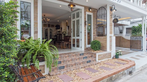 A hotel entrance with a stone facade, a wooden bench, and a gated driveway. - The Lek Aree (Bangkok)