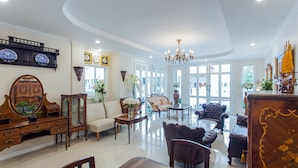 A spacious living room with a large chandelier, elegant furniture, and a view of the outdoors through large windows. - The Lek Aree (Bangkok)