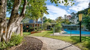 A pathway leading to a swimming pool with a fenced deck, surrounded by lush greenery and trees. - Brookfield Retreat (Brookfield)