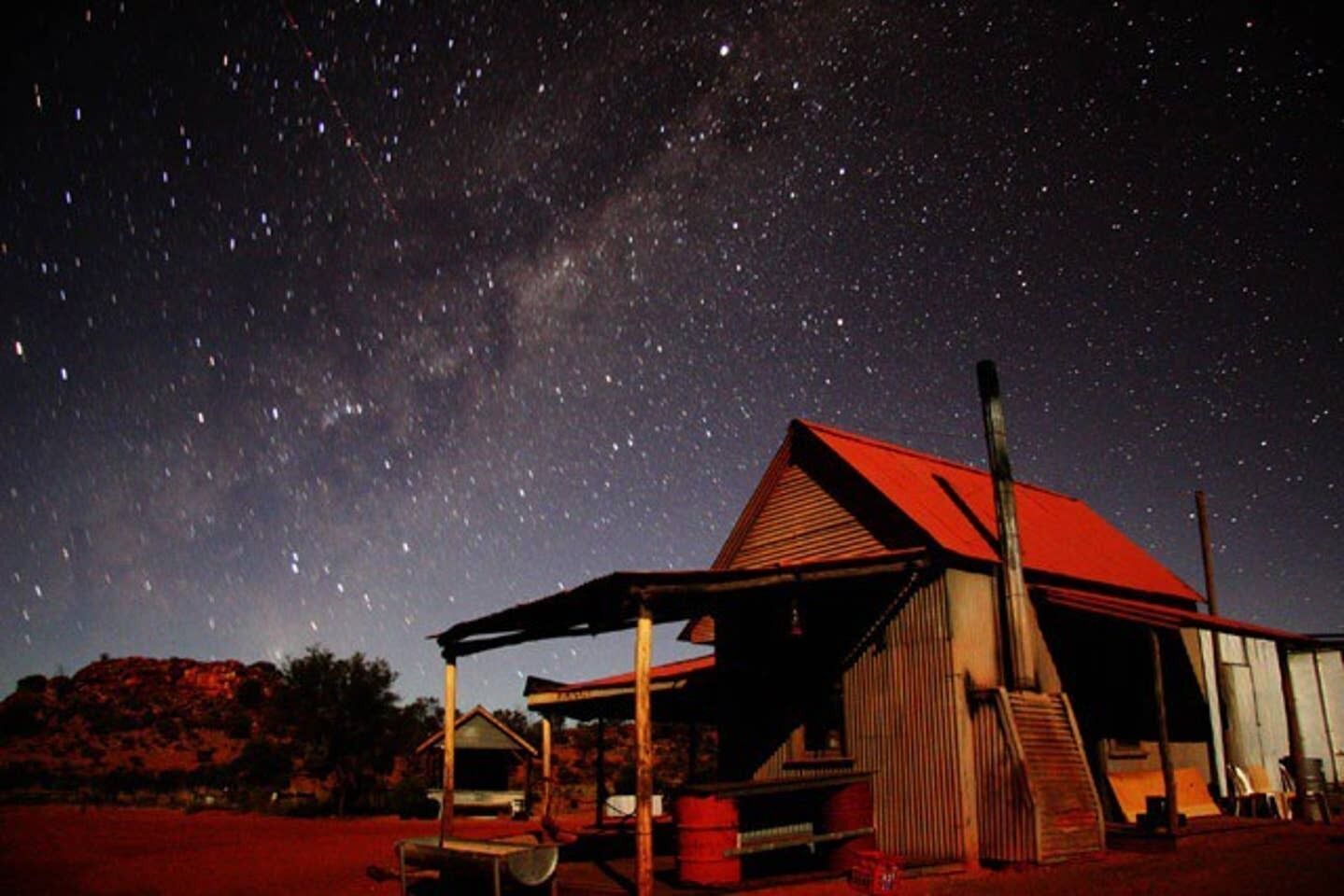 A rustic building with a red roof and a covered porch, surrounded by a natural landscape under a starry night sky.