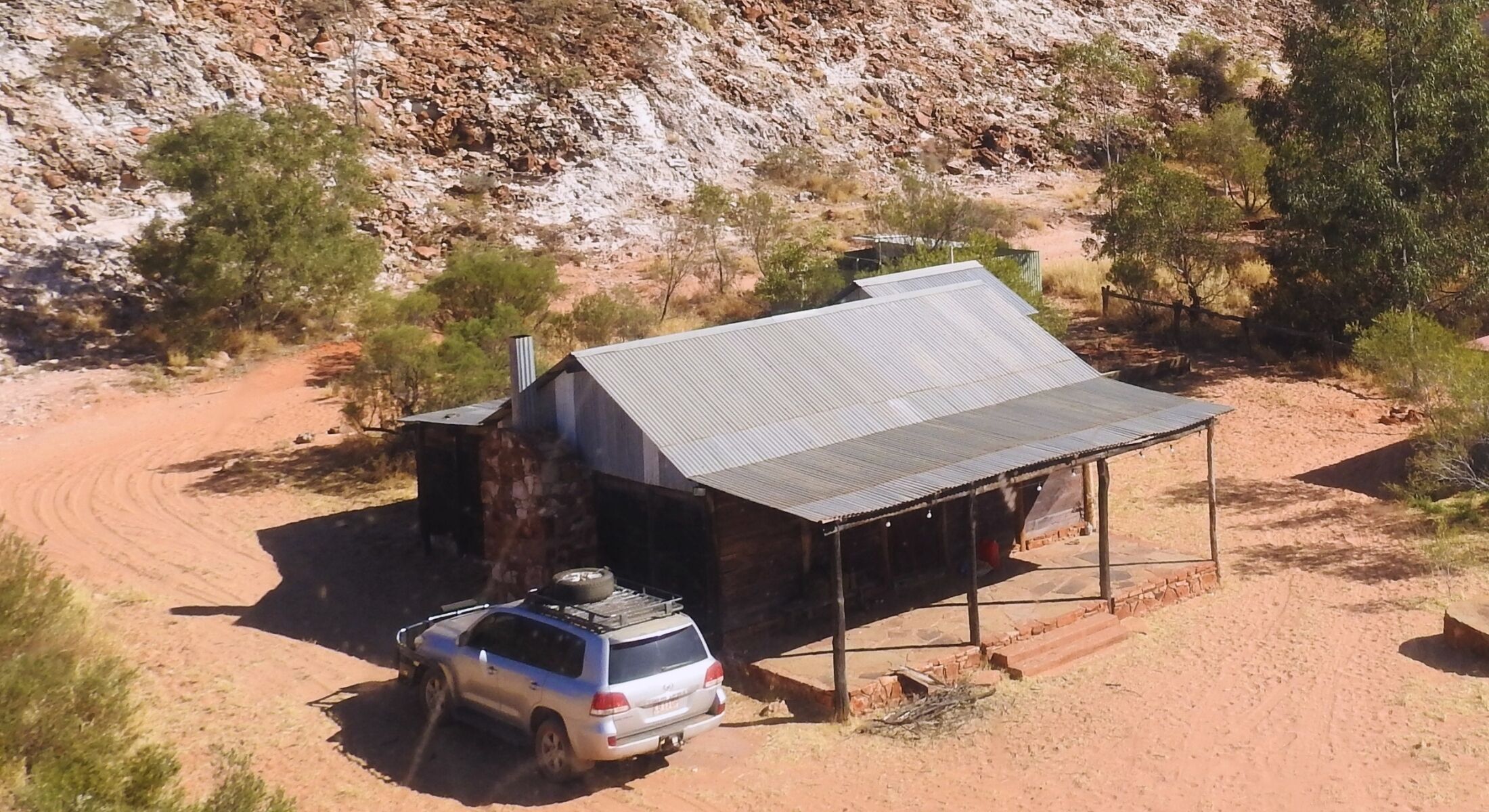 Una cabaña aislada con techo de metal, rodeada por un camino de tierra y vegetación escasa.