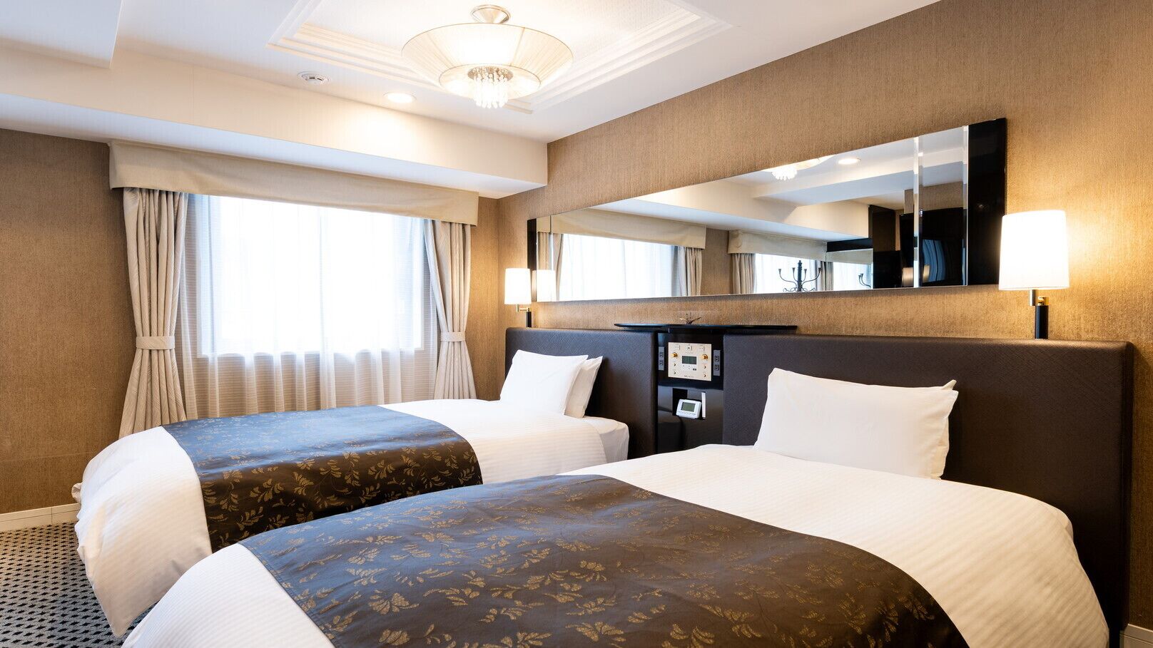 A hotel room with two beds, a large mirror, a bedside table with a clock, and a window with curtains.