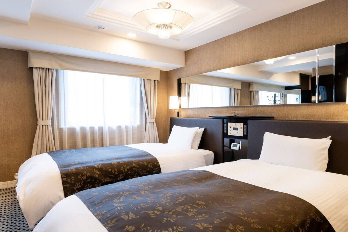 Hotelkamer met twee bedden, een grote spiegel, een nachtkastje met een klok en een raam met gordijnen.