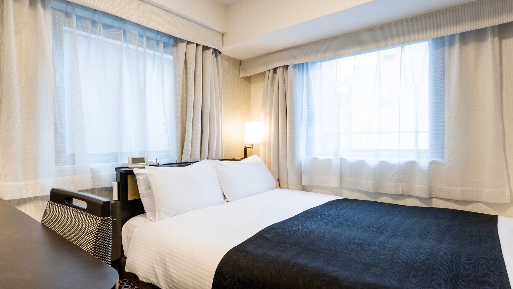 A hotel room with a large bed, a bedside table, a desk, and a chair.