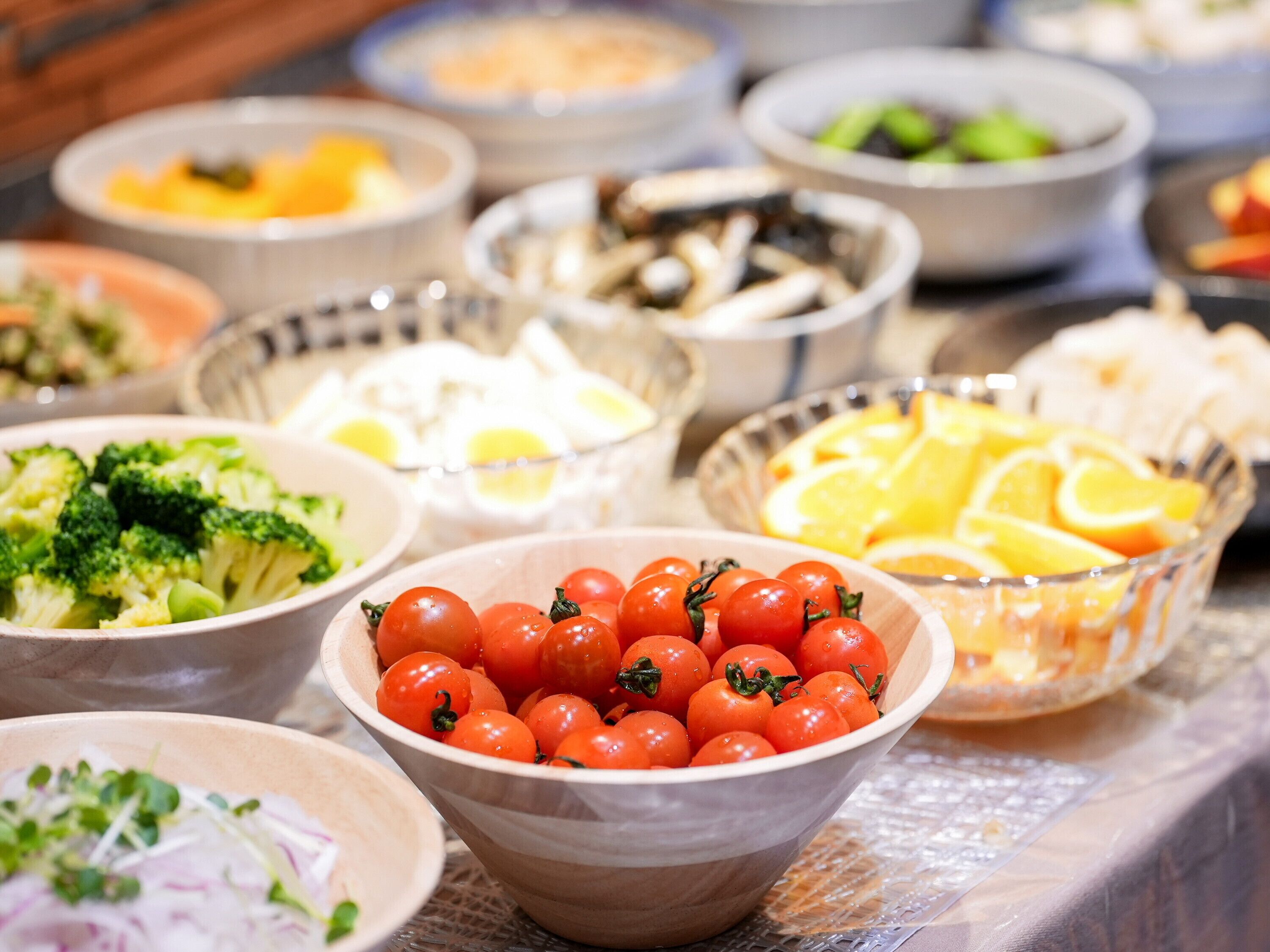 A variety of food items in bowls, including tomatoes, broccoli, and sliced oranges.