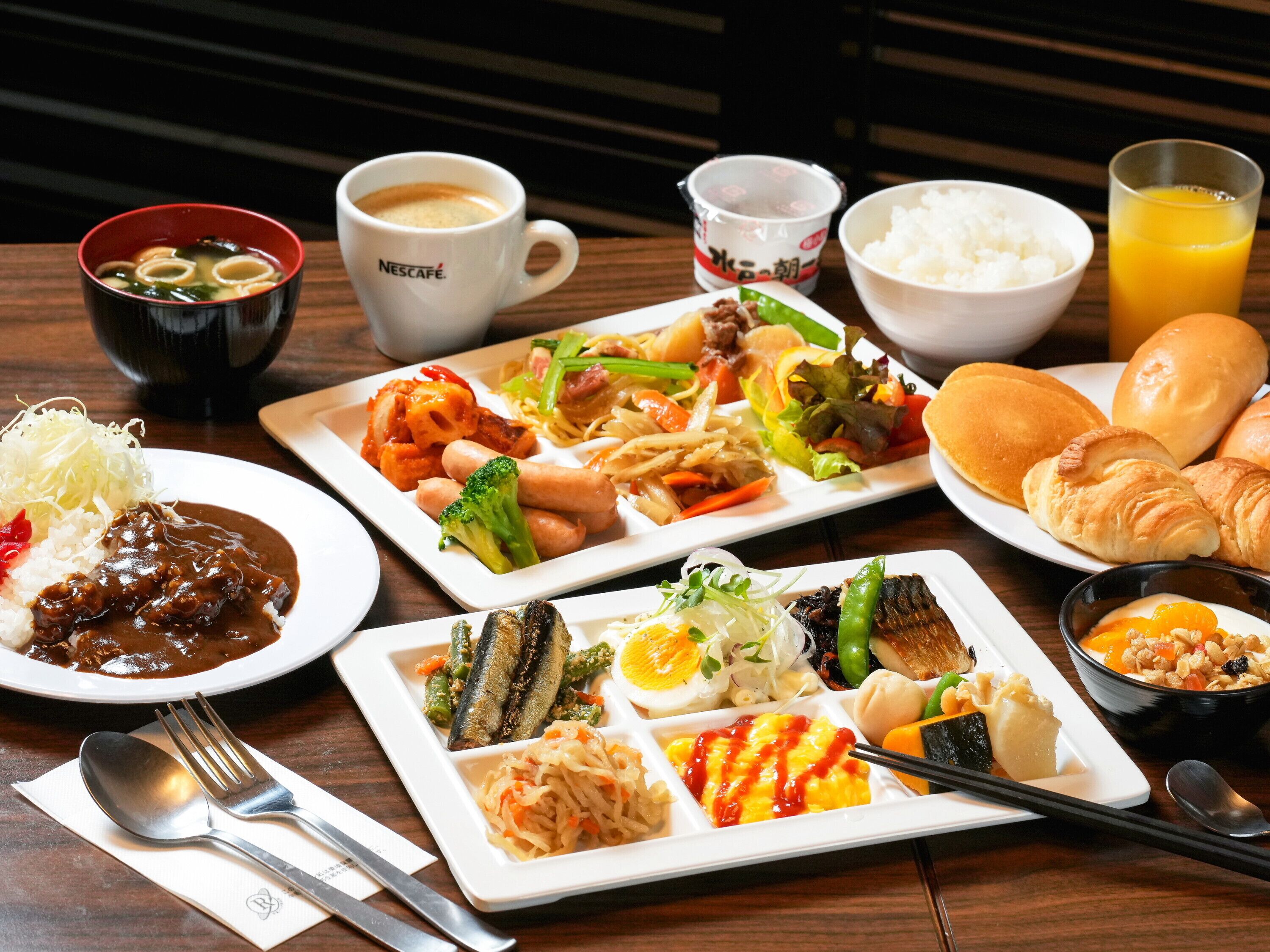 Diversos platos que incluyen arroz, fideos y verduras, junto con bebidas y pan sobre una mesa de madera.