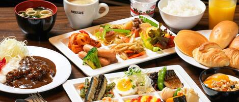 Diversos platos que incluyen arroz, fideos y verduras, junto con bebidas y pan sobre una mesa de madera.