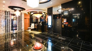 Um hall moderno com piso lustroso, um candelabro central e uma área de recepção com visor digital.