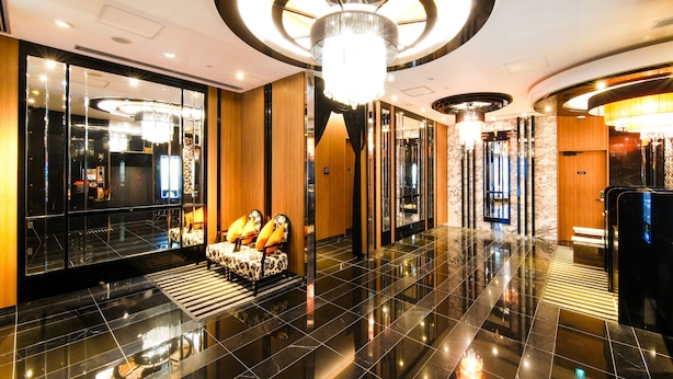 Um lobby moderno com piso preto refletivo, área de estar central com cadeiras estampadas e um grande luminário circular no teto.