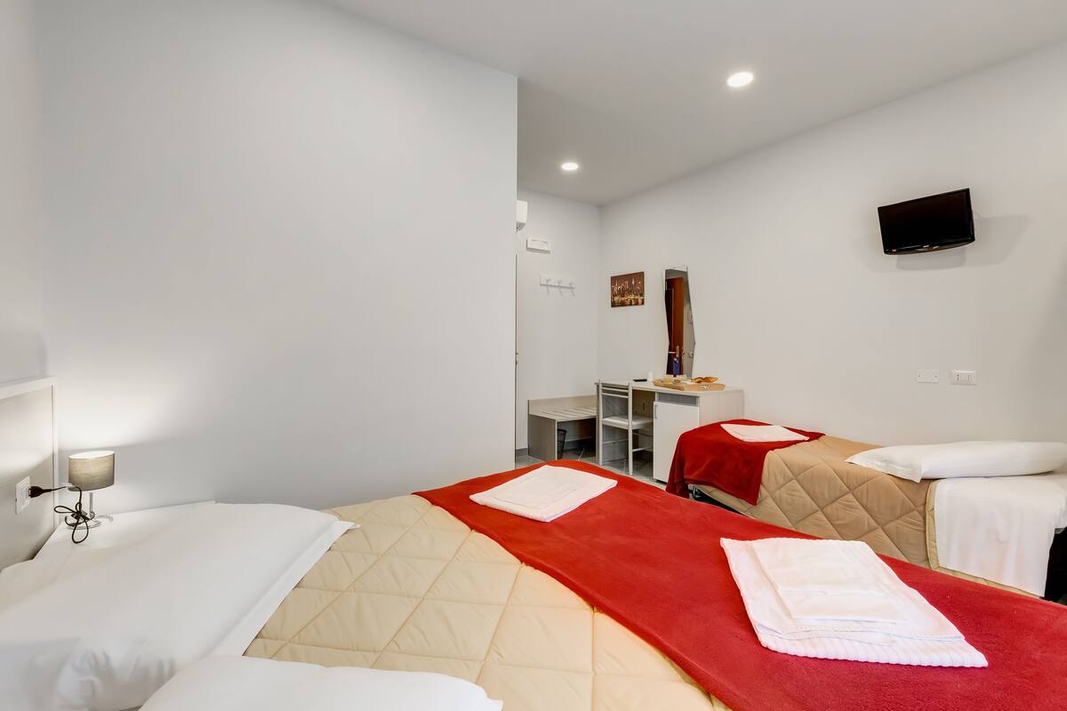 A hotel room with two beds, a desk, a TV, and a mirror.