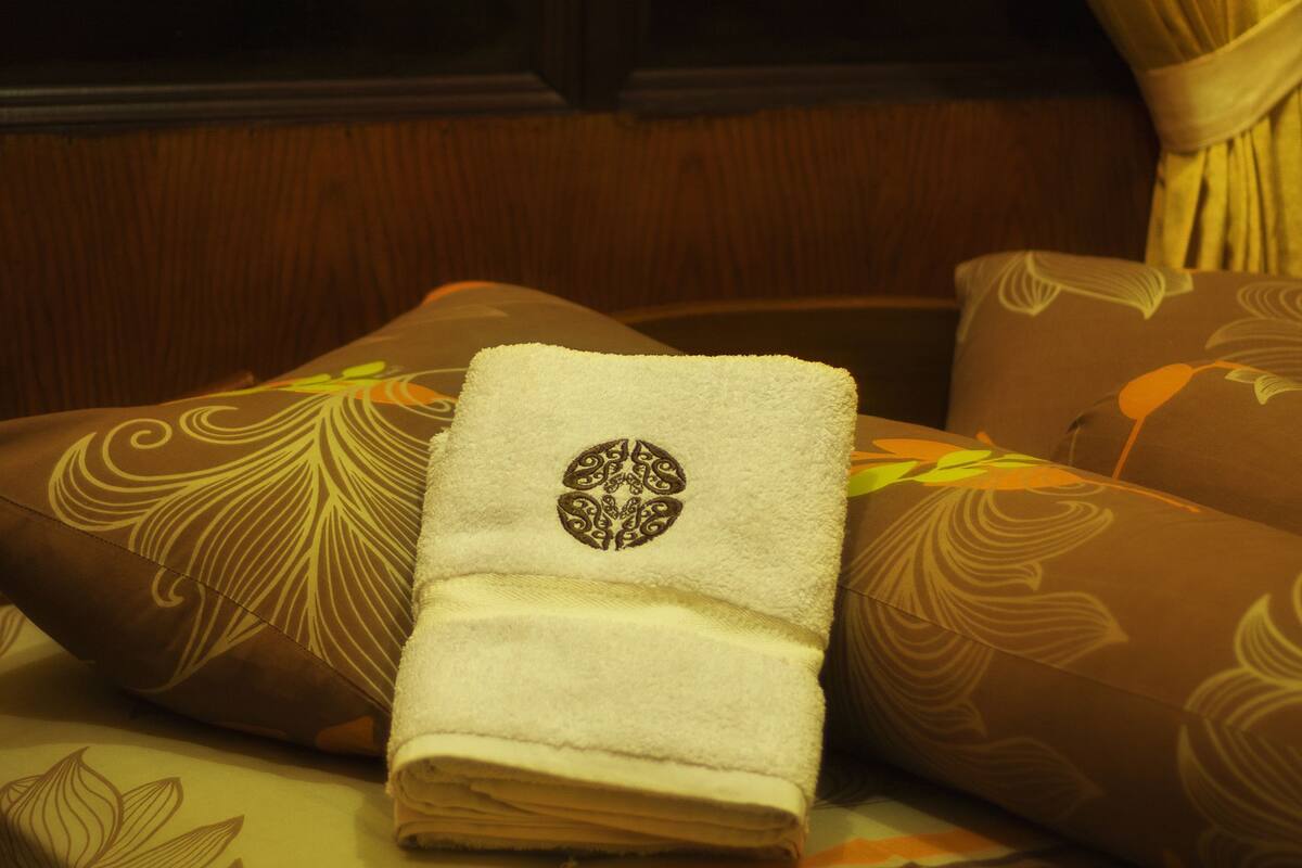 A bed with a folded towel, patterned pillows, and curtains.