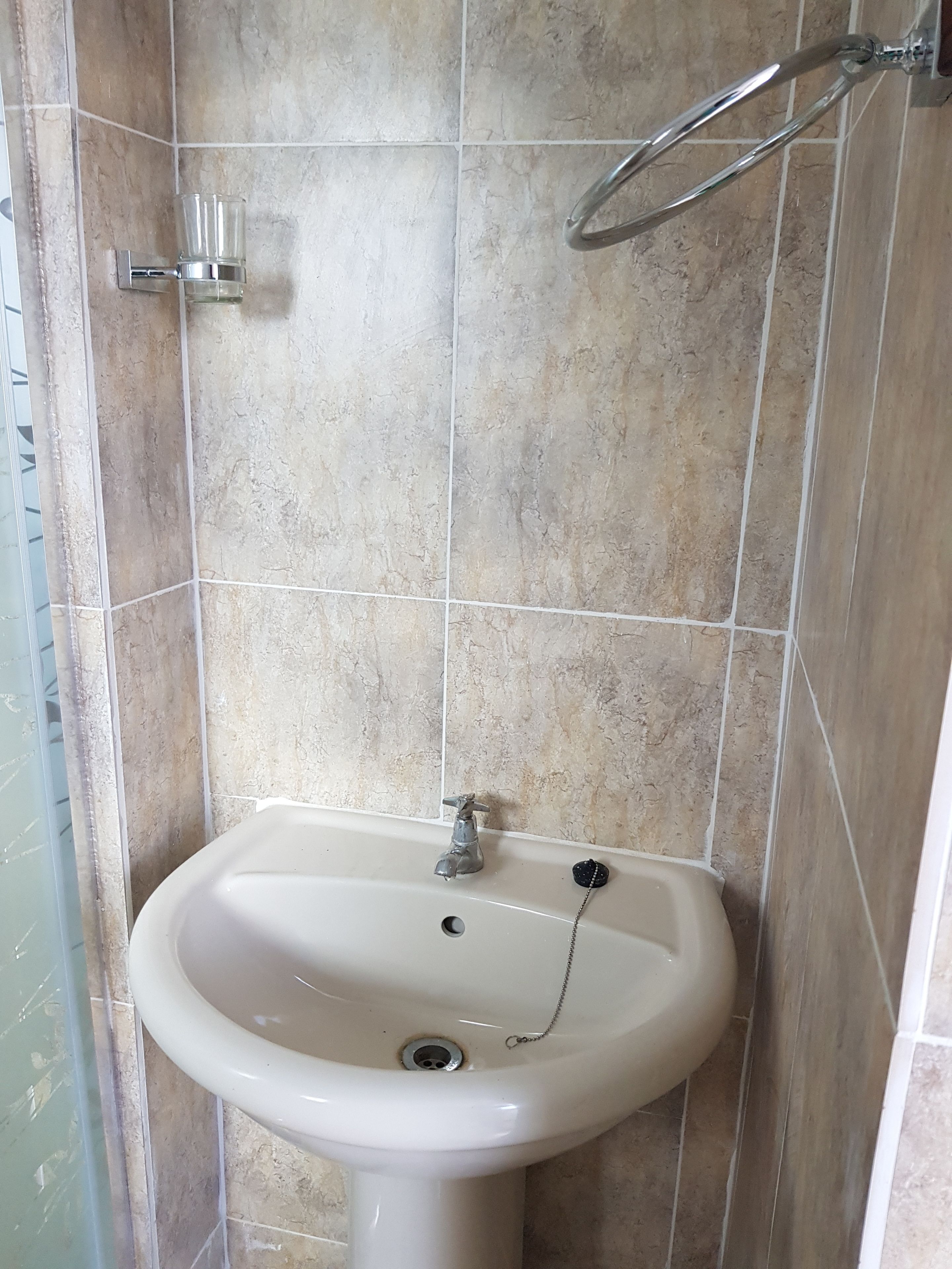 Un baño con lavamanos blanco, cabezal de ducha y paredes con azulejos.