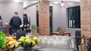 A modern dining area with brick accents, a central table with chairs, and a buffet with fruits and glasses. - Chinyonga Guesthouse (Blantyre)