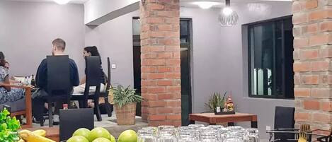 A modern dining area with brick accents, a central table with chairs, and a buffet with fruits and glasses.