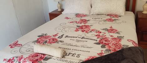A neatly made bed with a floral bedspread, two bedside tables with lamps, and a wooden headboard.