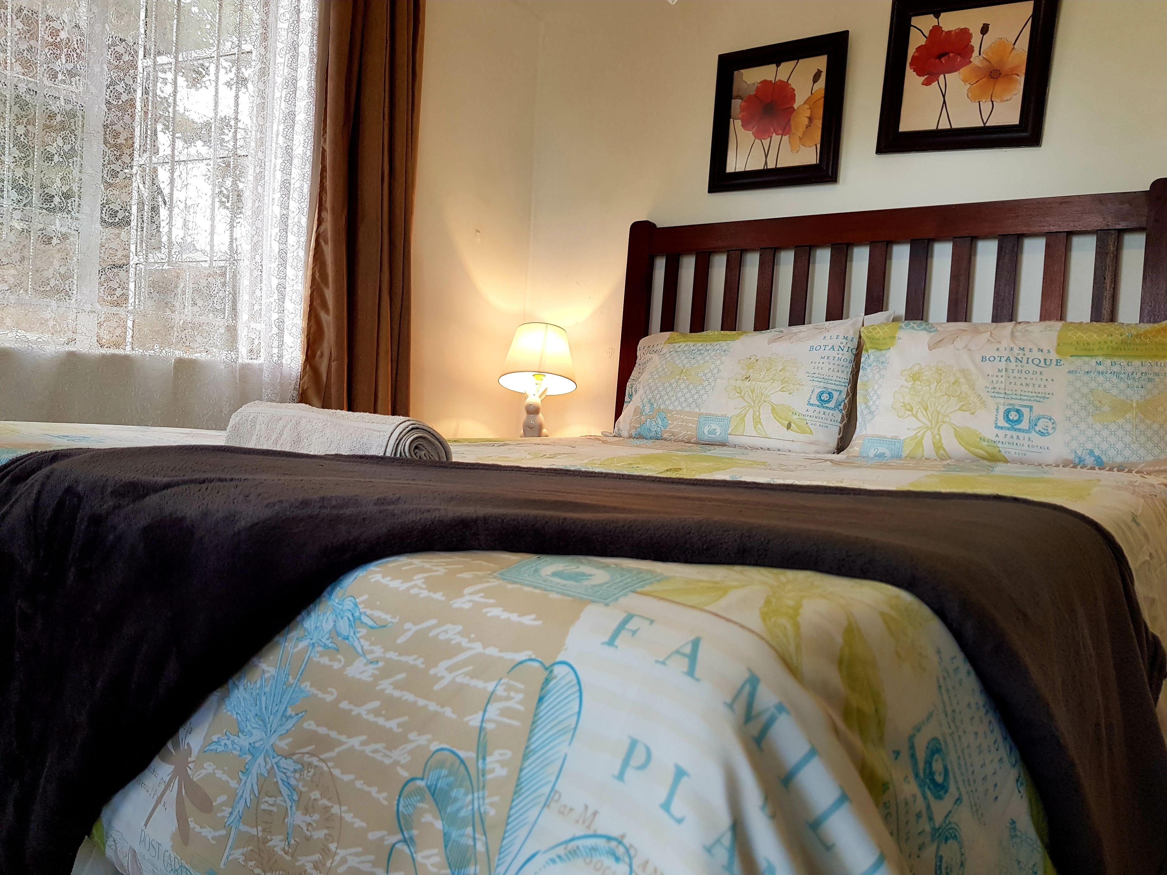 A hotel room with a bed, a lamp, and two framed floral paintings on the wall.