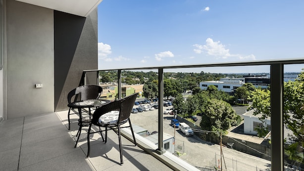 A balcony with a table and chairs, overlooking a parking area and buildings. - Poplar Sanctuary Apartments (Box Hill)