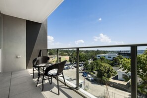 A balcony with a table and chairs, overlooking a parking area and buildings. - Poplar Sanctuary Apartments (Box Hill)