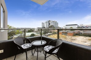 A balcony with two wicker chairs and a small round table, overlooking a construction site and residential buildings. - Poplar Sanctuary Apartments (Box Hill)