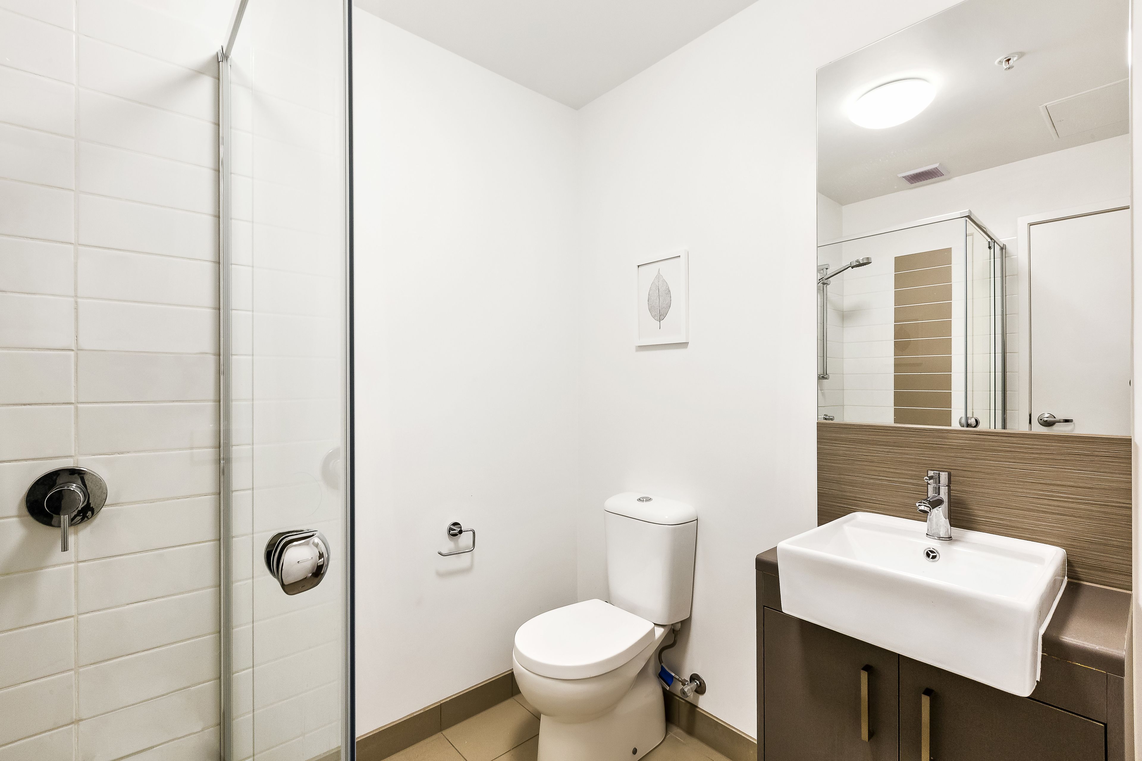 A modern bathroom with a glass shower enclosure, a white toilet, and a sink with a mirror above it.