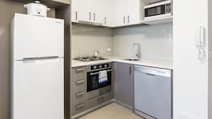 A modern kitchen with a white refrigerator, stainless steel oven, microwave, and dishwasher. - Poplar Sanctuary Apartments (Box Hill)