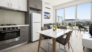 A modern kitchen with a dining area, large windows, and a view of the city. - Poplar Sanctuary Apartments (Box Hill)