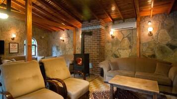 Una habitación acogedora con paredes de piedra, vigas de madera, chimenea y asientos cómodos.