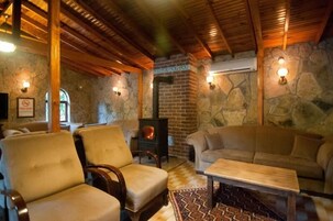 Una habitación acogedora con paredes de piedra, vigas de madera, chimenea y asientos cómodos.